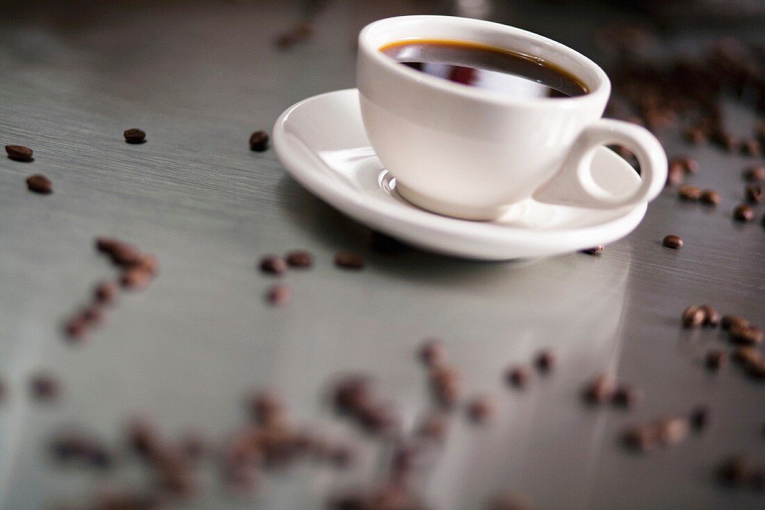 A cup of coffee surrounded by coffee beans