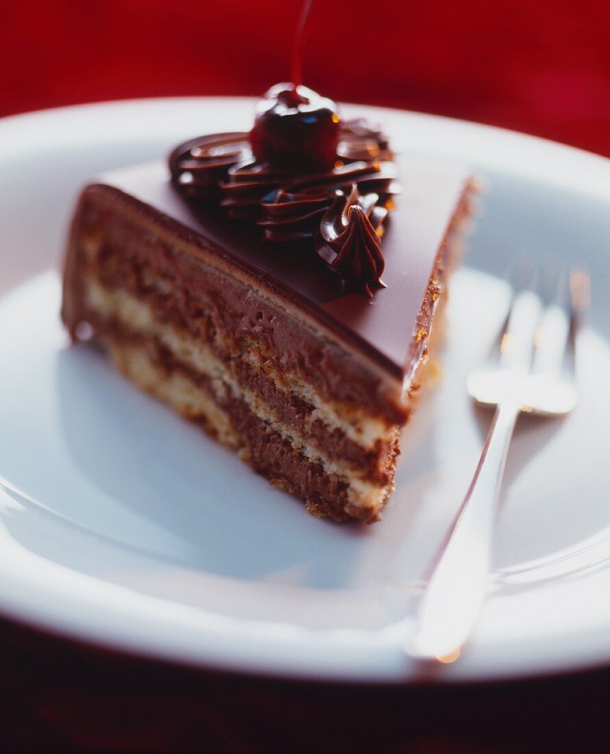 A slice of chocolate layer cake topped with cherries