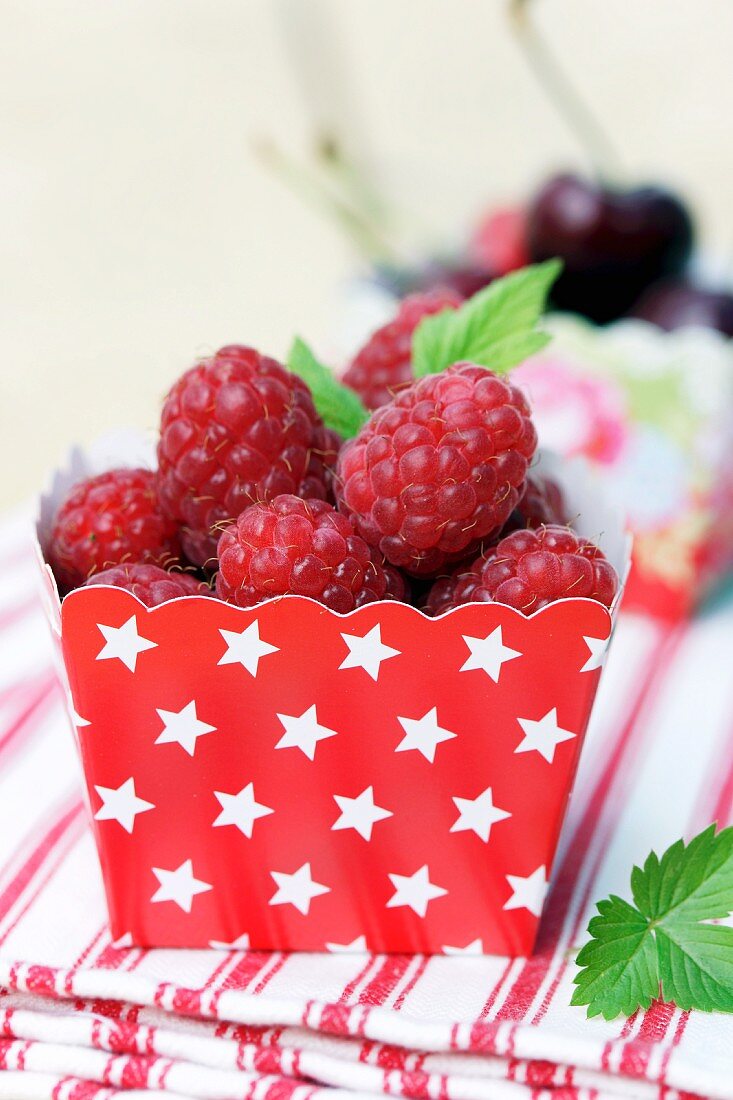 Fresh raspberries in red cardboard punnet with pattern of white stars
