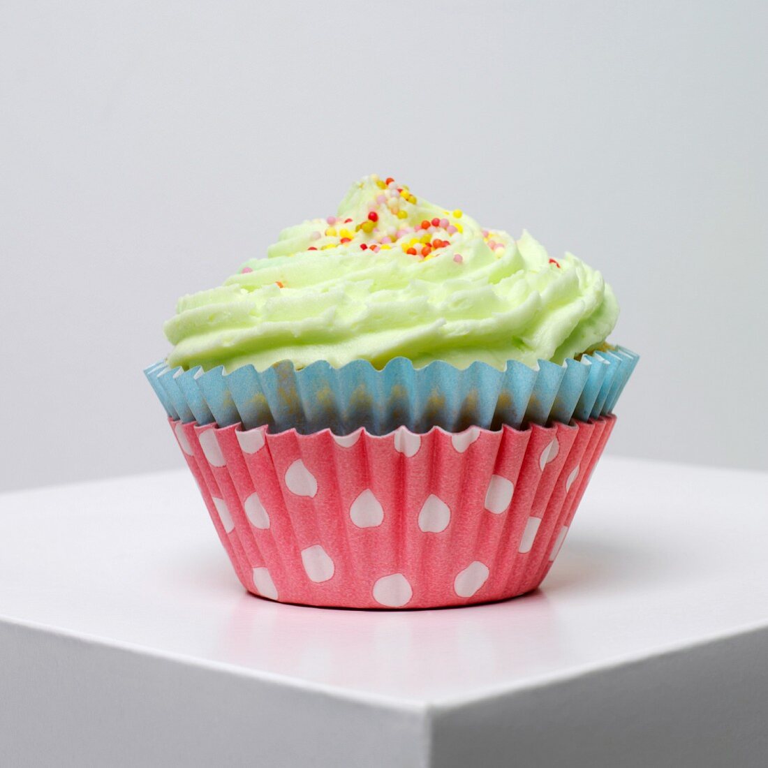 A cupcake with pistachio icing and colourful sugar balls