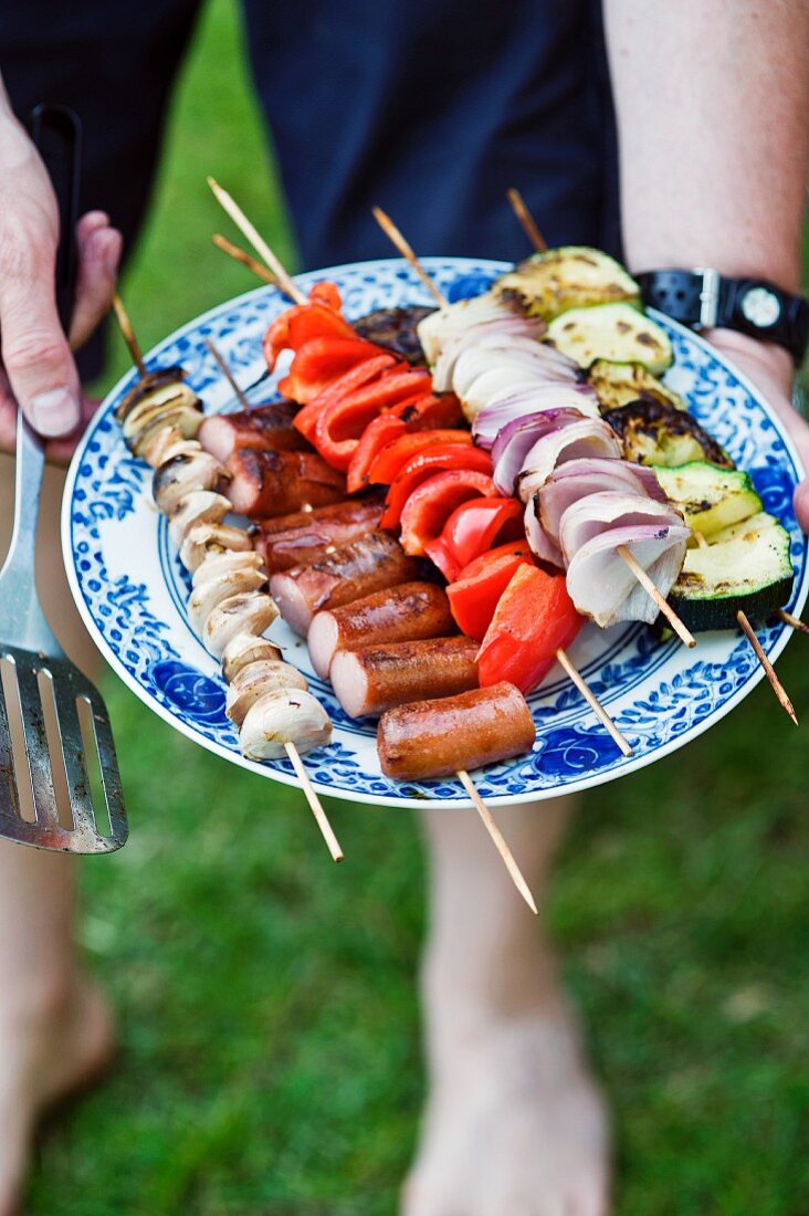 Man holding skewers on plate