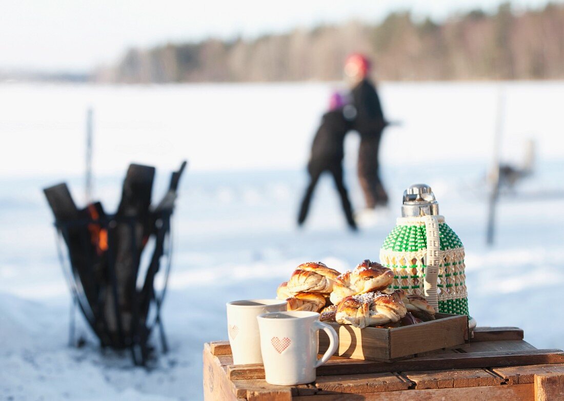 Table with thermos, sweet buns and mugs, people in background