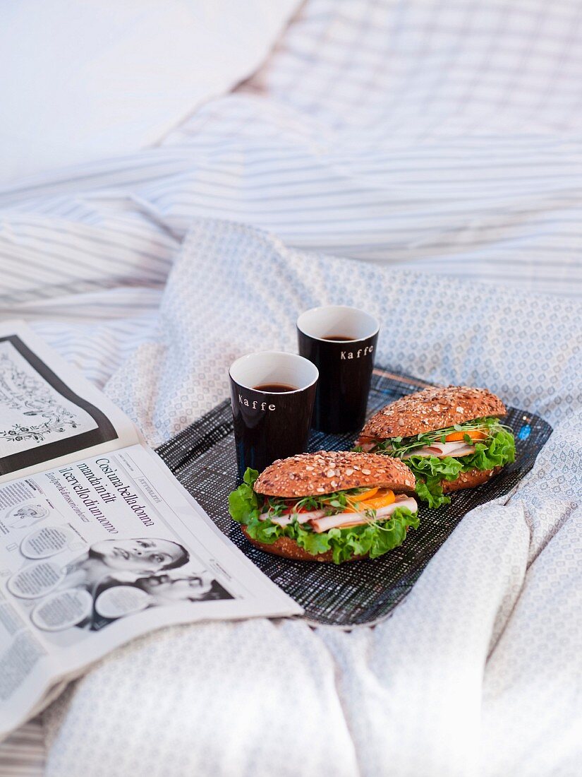 Frühstück im Bett mit Sandwiches, Kaffee und Zeitung
