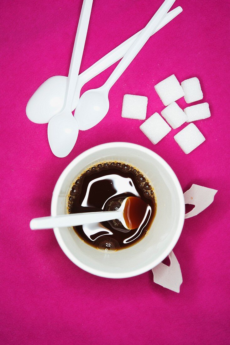 Kaffeetasse, Zuckerwürfel und Plastiklöffel