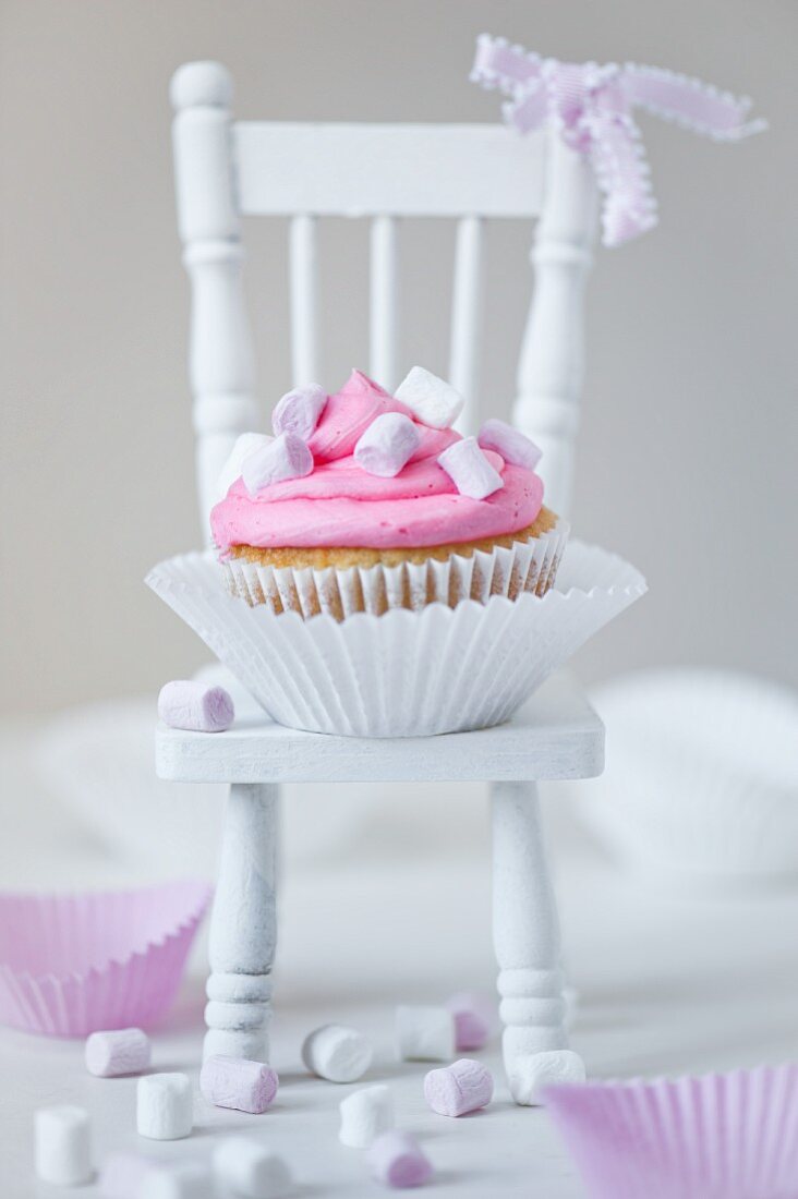 Marshmallow-Cupcake mit rosa und weißen Marshmallows auf weißem Puppenstuhl mit rosa Schleife
