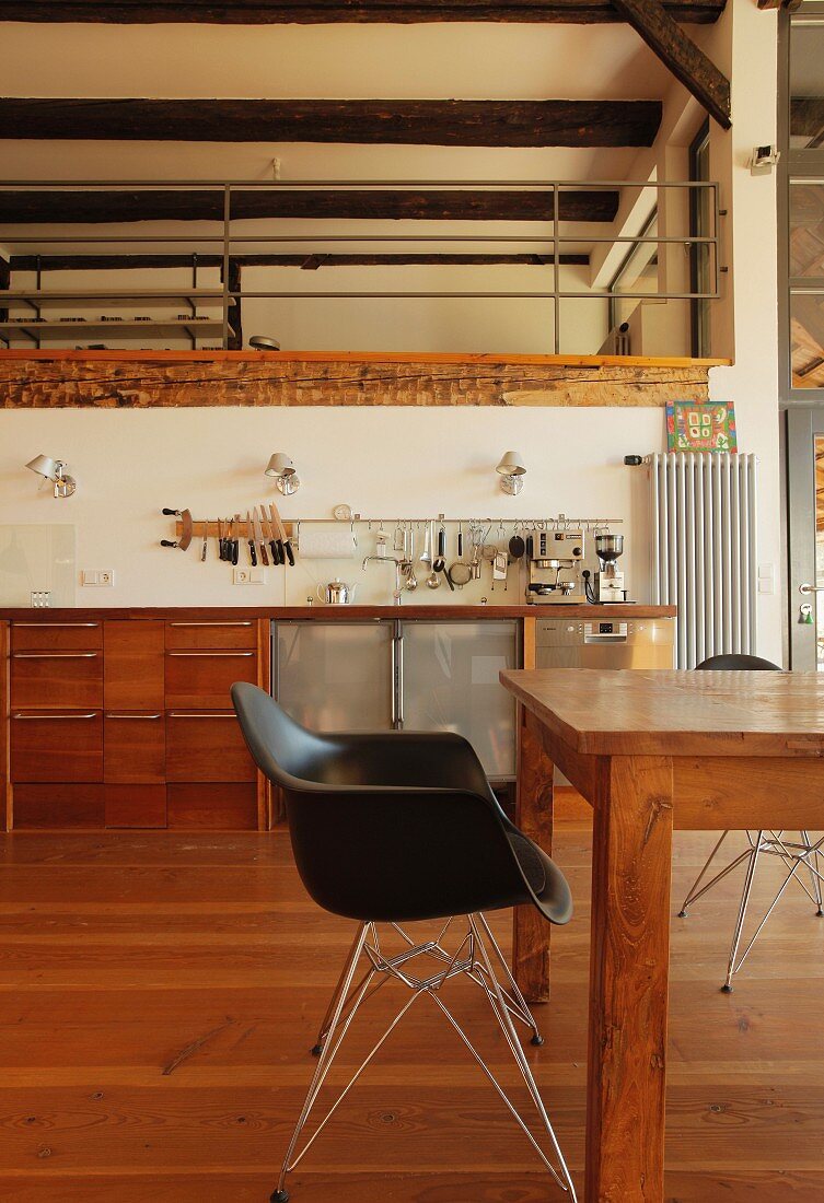 Black shell chair with metal frame at wooden table in front of kitchen counter in open-plan interior