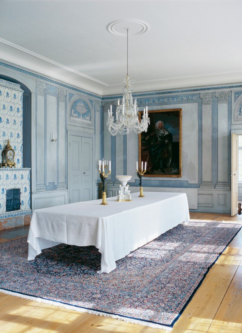 Grand dining room with painted wooden panels on walls and long dining table with white tablecloth below chandelier