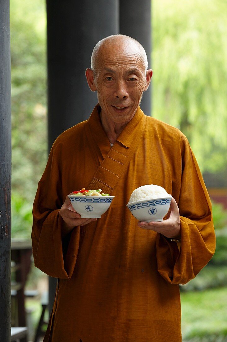 A monk with a bowl of rice and a bowl of vegetables