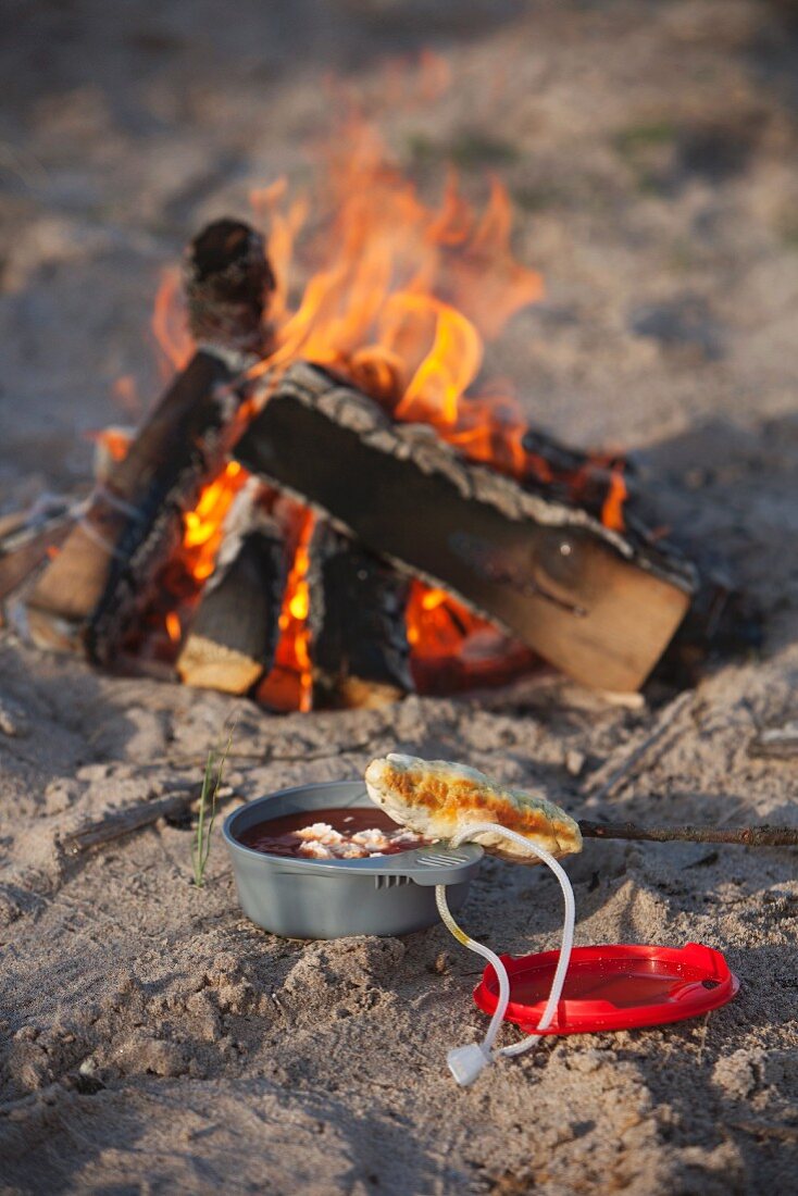 Soup in camping bowl next to open fire on beach