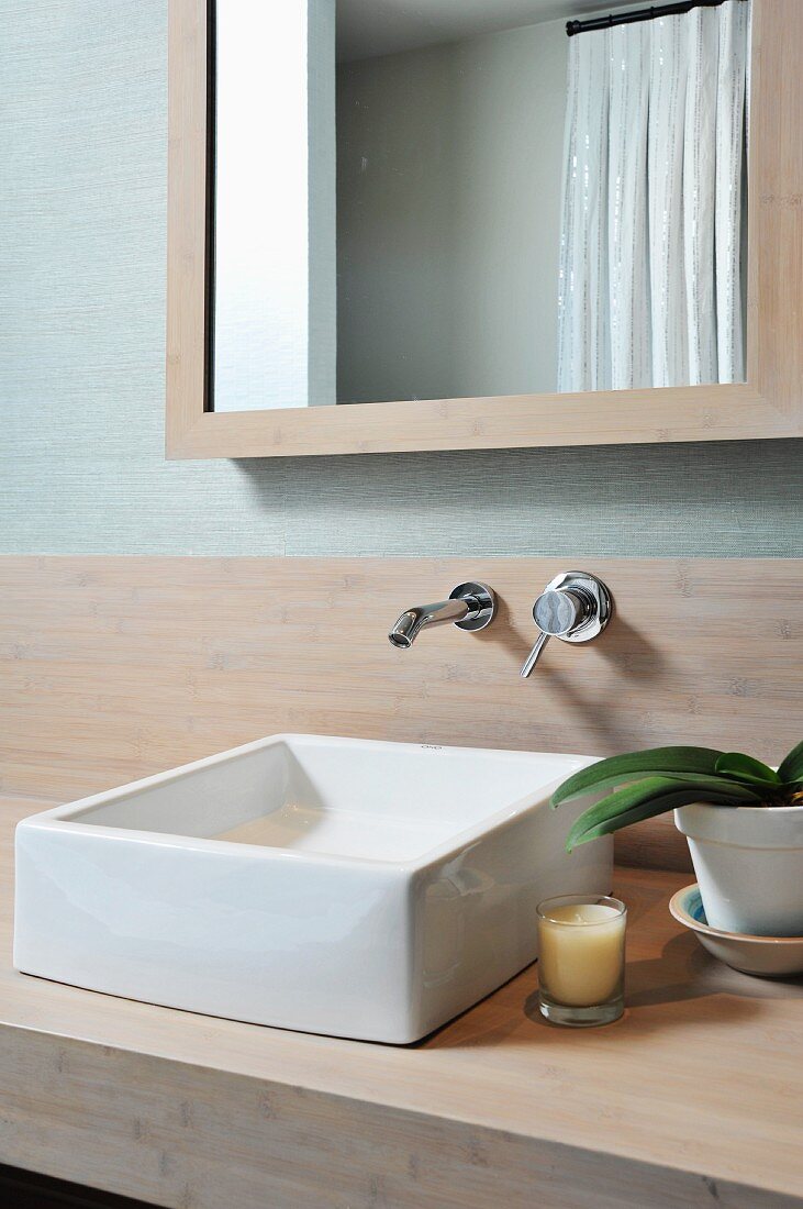 White washbasin on wooden surface below wall-mounted taps and framed mirror