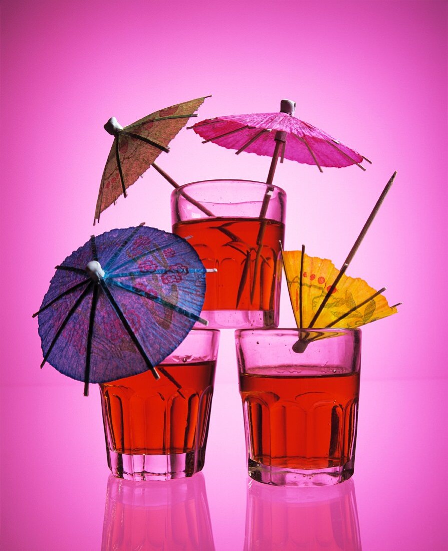 Drei Drinks mit Papierschirmchen vor pinkem Hintergrund
