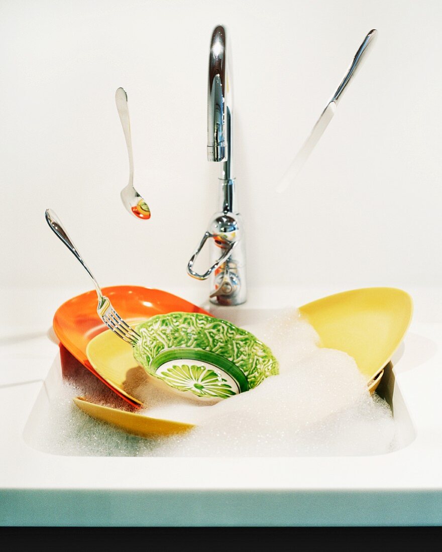 Cutlery falling into a kitchen sink full of washing-up water and dishes