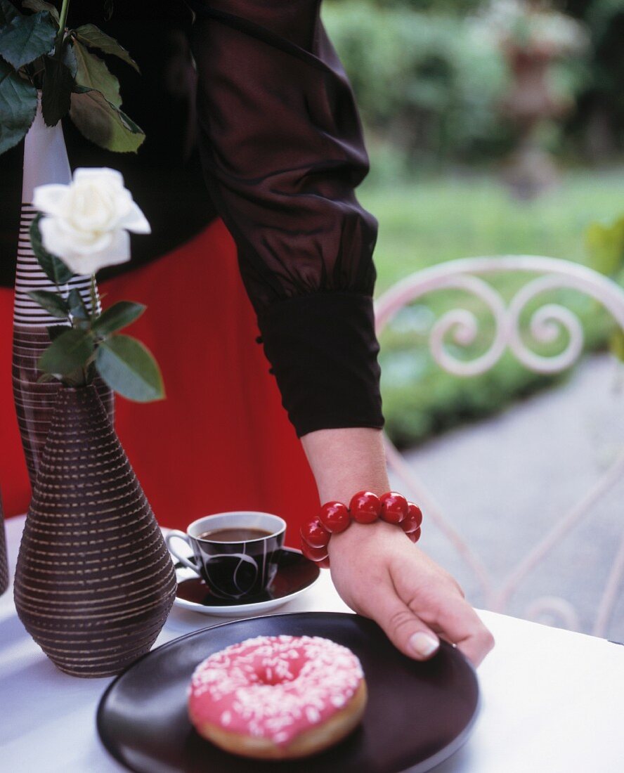 A woman putting a plate with a doughnut on it on a table in the garden