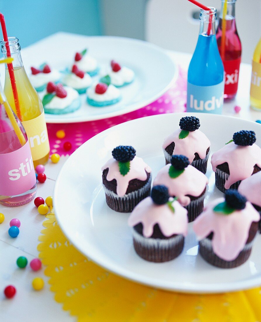 A table at a children's party with mini cakes and bottles of pop