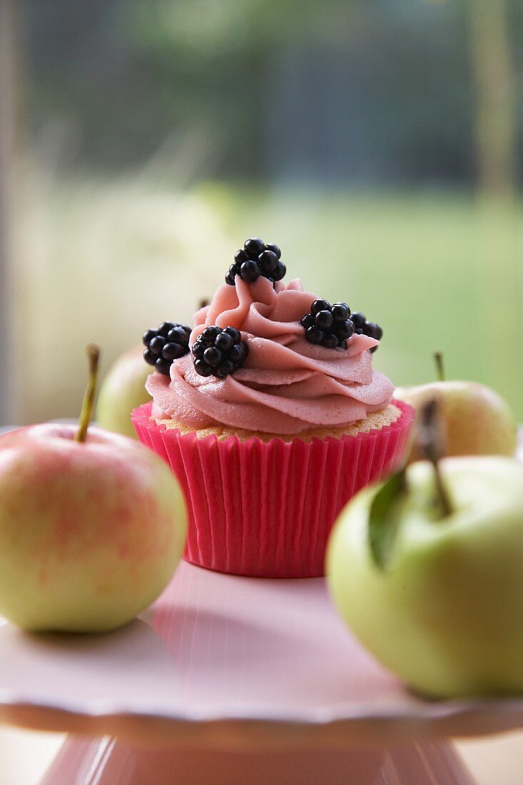 Cupcake mit Brombeeren, umgeben von frischen Äpfeln