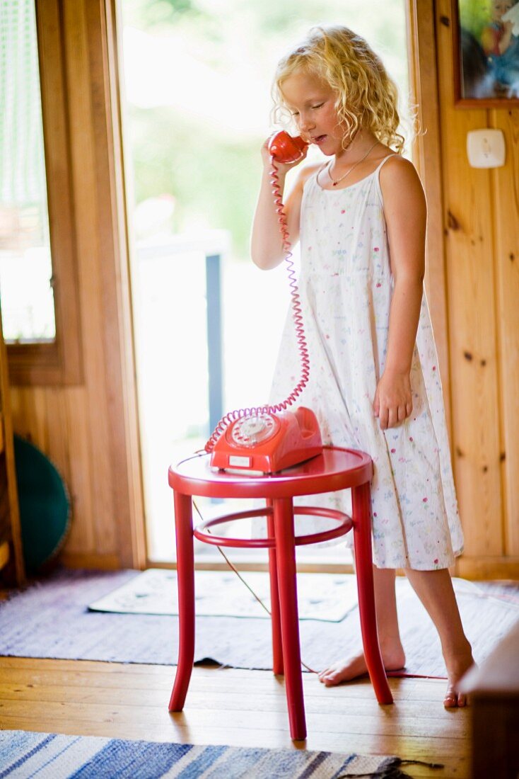 Mädchen im Sommerkleid beim Telefonieren mit Retro-Telefon