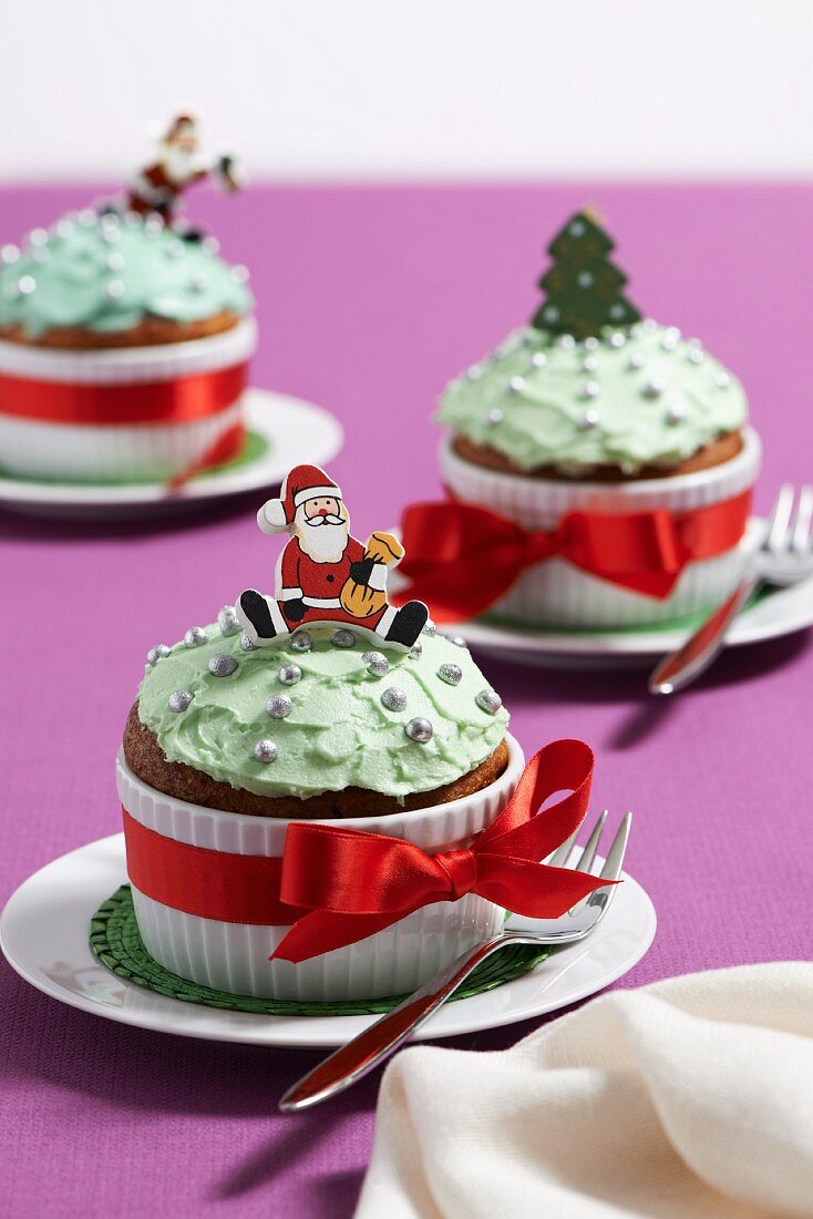 Buttercreme-Cupcakes in einem Becher mit roter Schleife, Weihnachtsmann und Tannenbaum