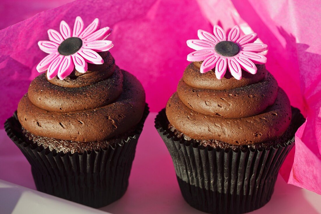 Schokoladencupcakes mit Karamellfüllung, Schokoladencreme und pinken Zuckerblumen