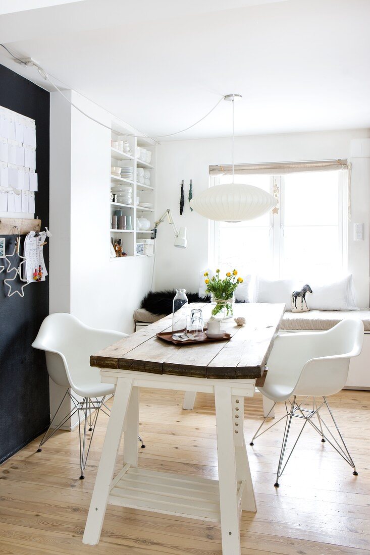 White, classic chair and old table top on white trestles; shelves in niche and window seat in background