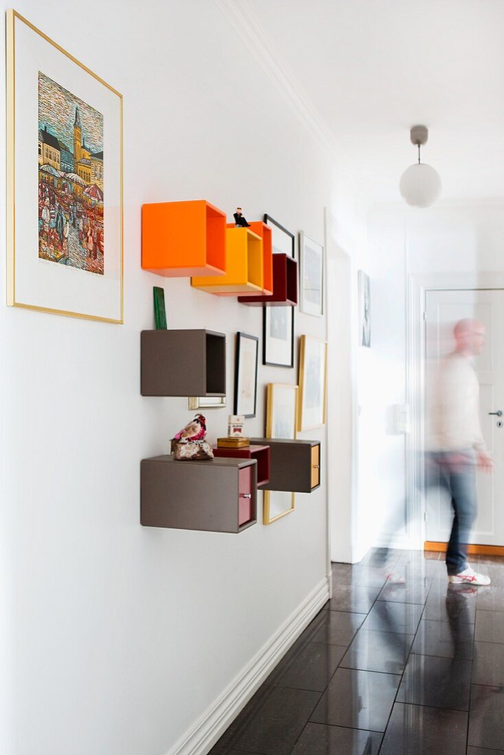Colourful, cubic shelving units on wall in hallway; man in background