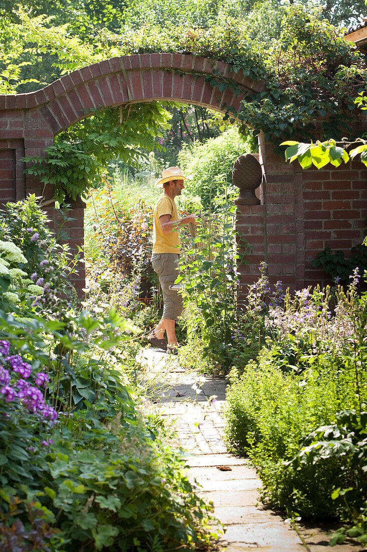 Flowering garden; man below brick archway in background