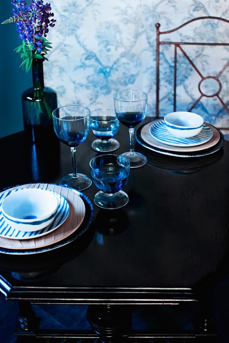 Two place settings with glasses and bottle of lupins on antique table