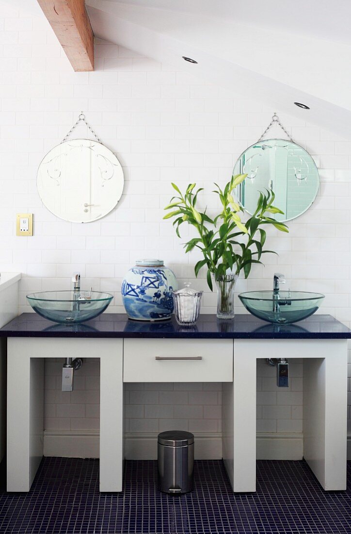 Twin washstand with glass basins and round mirrors on white, tiled wall