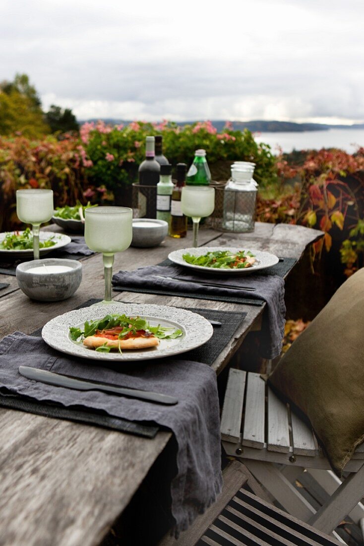 Autumnal atmosphere; pizza and salad on table with rustic place settings and view of Norwegian skerry coast