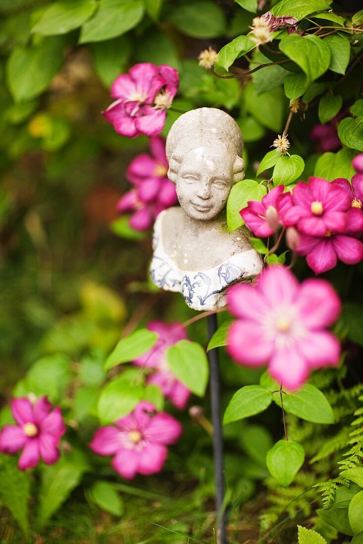 Mädchenbüste auf Metallstab zwischen rosaroten Gartenblumen