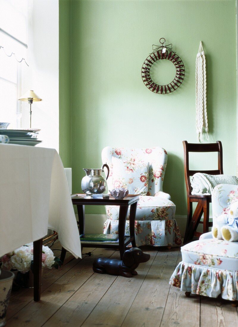 Seating area in green-painted interior with floral upholstered armchairs & side table