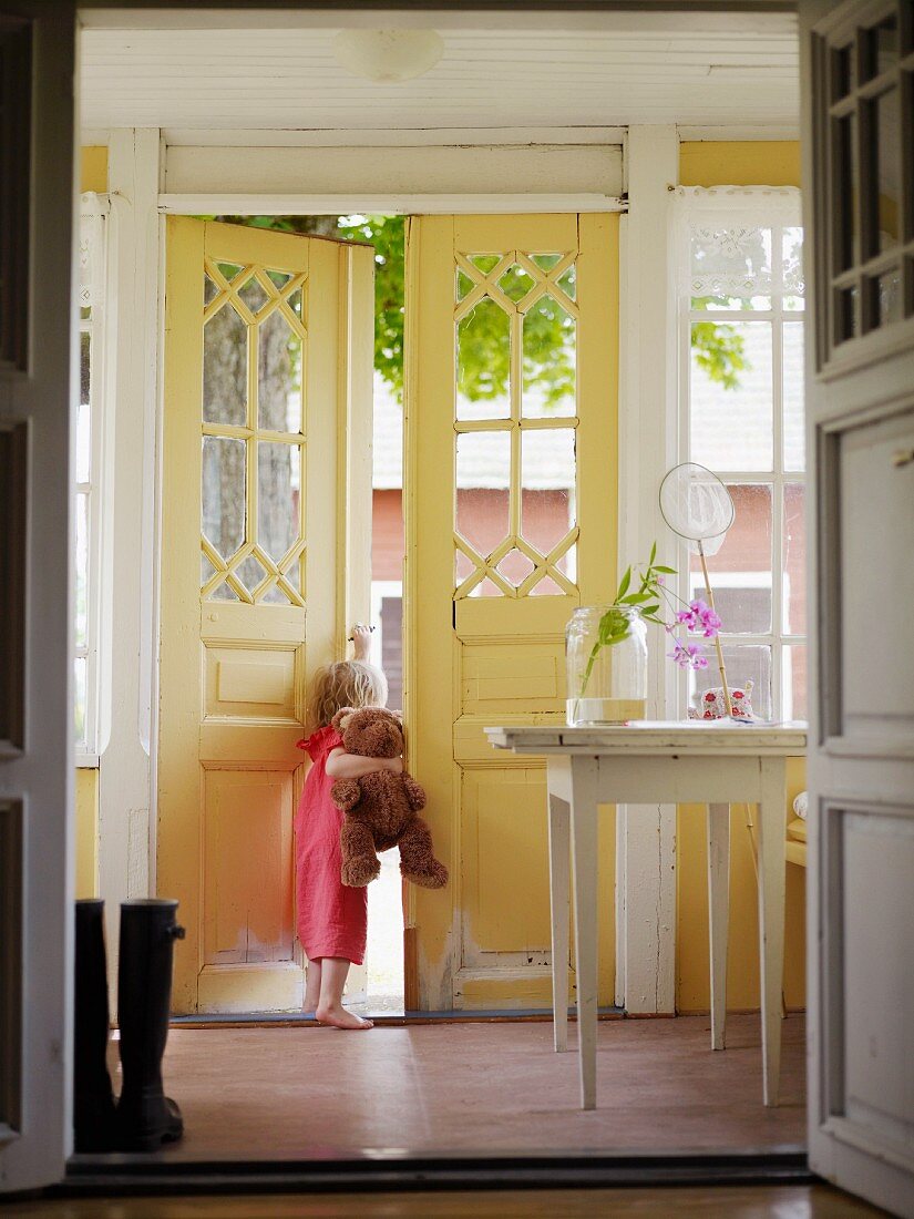 Little girl holding teddy bear looking out of open front door