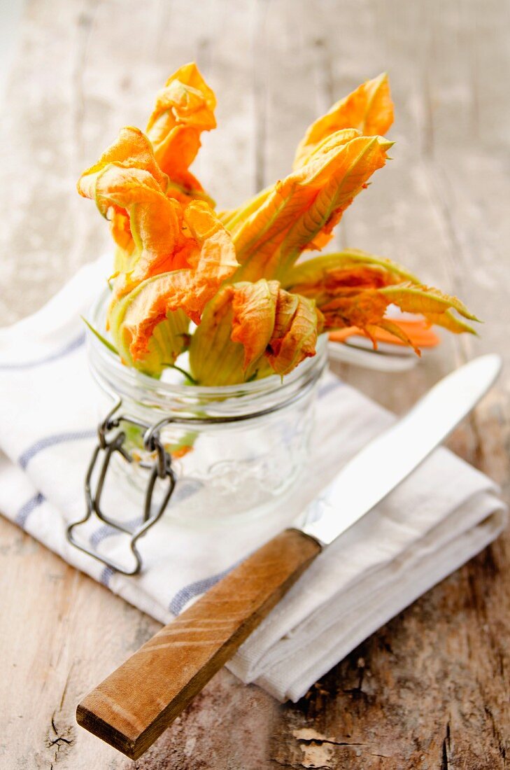 Zucchiniblüten in einem Weckglas auf Geschirrtuch mit Messer
