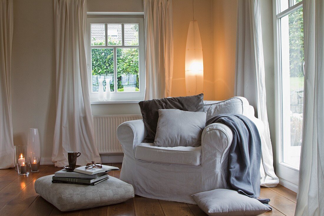 Comfortable armchair, floor cushions and elliptical lamp in corner of living room