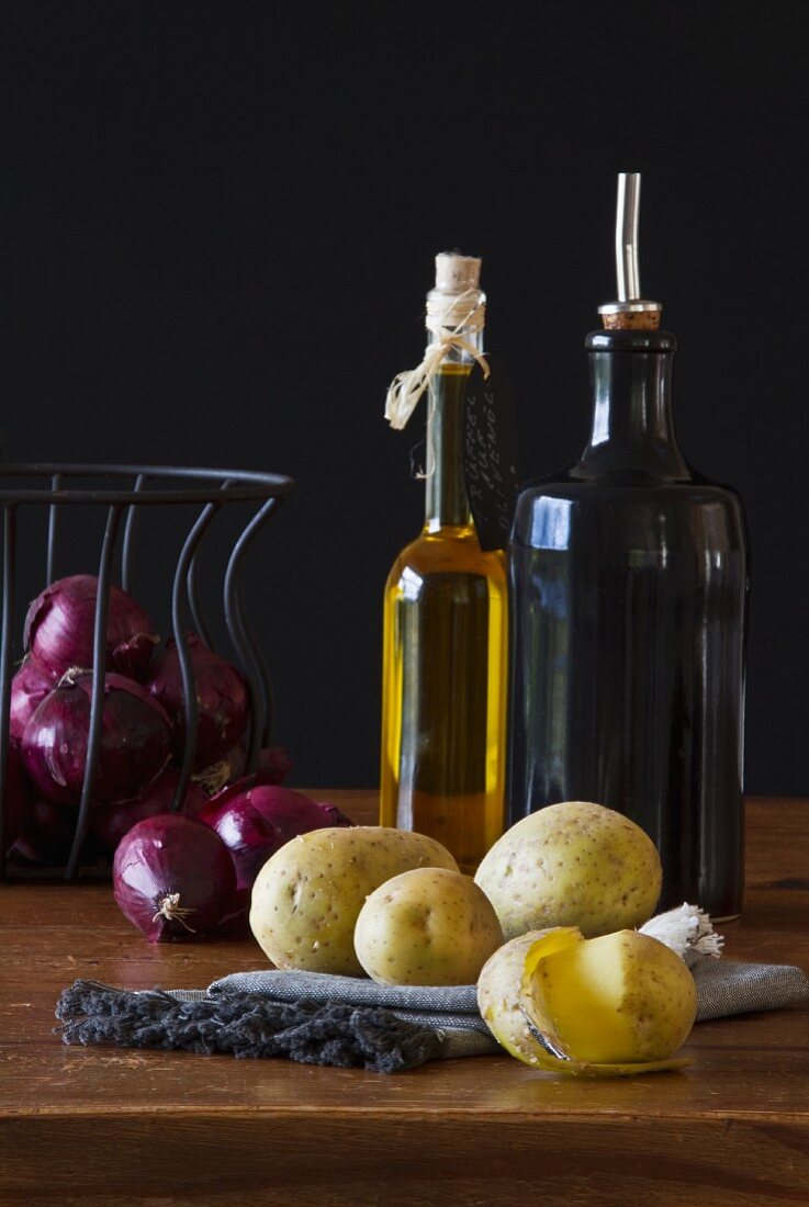 Still-life arrangement of red onions, potatoes, vinegar and oil