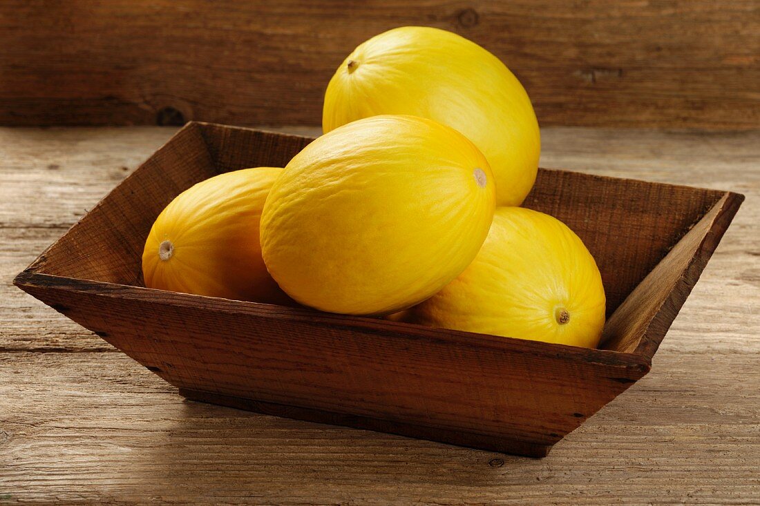 Several honeydew melons in a wooden bowl