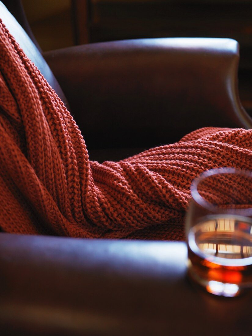 A Leather arm chair with a cable knit throw and glass of bourbon