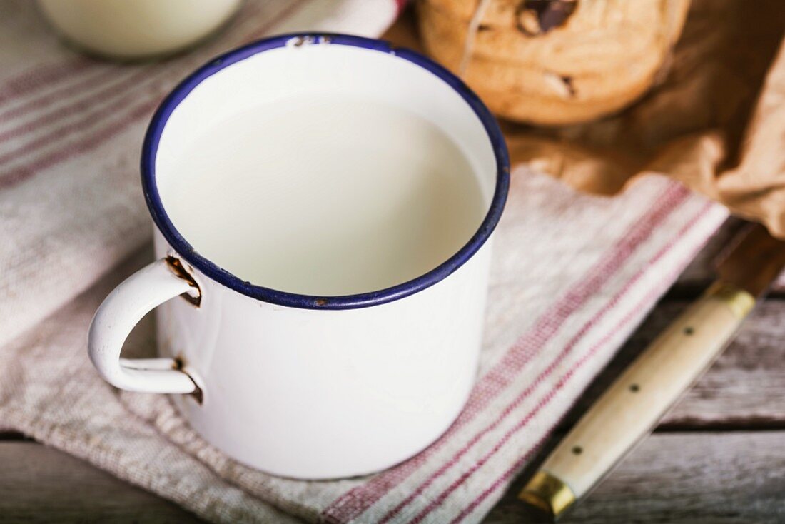 Frische Milch im Emaillebecher und Cookies auf rustikalen Holztisch