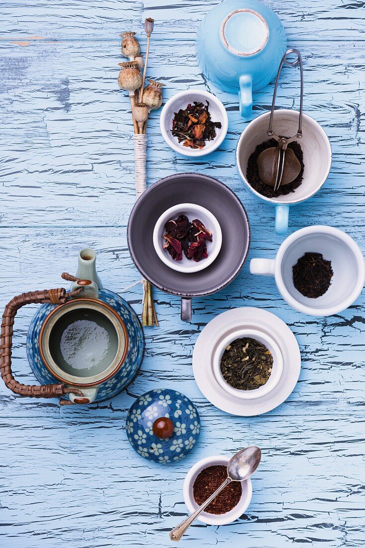 A still life featuring assorted types of tea, a teapot and a tea strainer