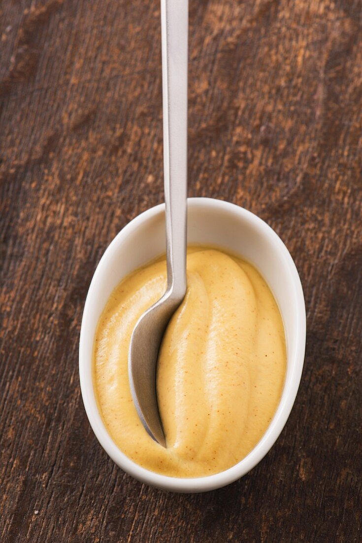 Closeup of dijon mustard in a white bowl and a spoon.