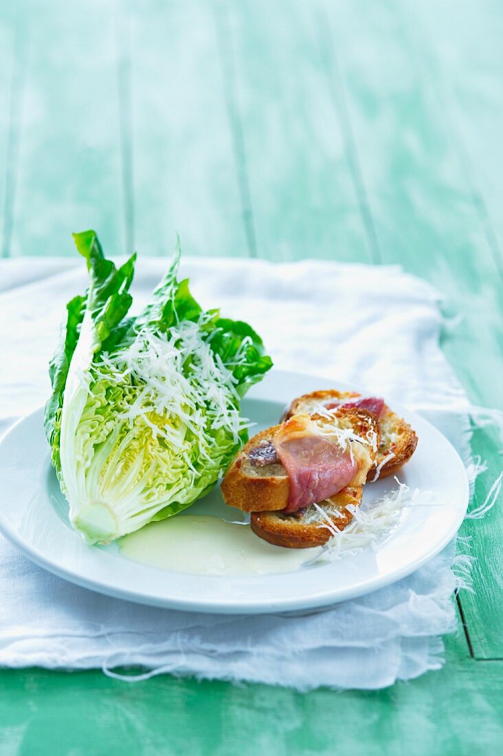 Blattsalat mit geriebenem Käse, Joghurtdressing und geröstetem Baguette mit Speck