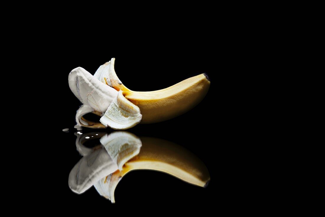 Geschälte Banane begossen mit flüssigem Make-Up vor schwarzem Hintergrund