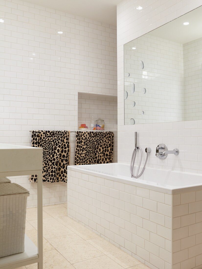 White-tiled bathroom with large mirror above bathtub and leopard-patterned towels