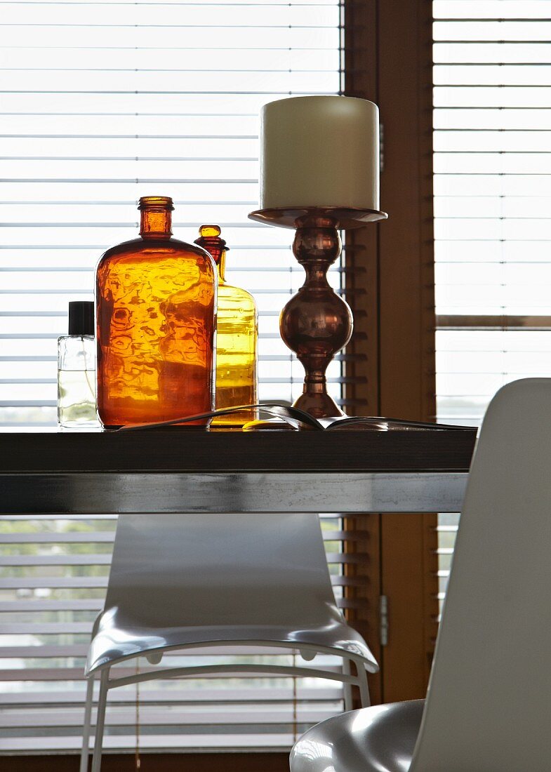 Großer, antiker Kerzenhalter neben braunen Vintage-Flaschen auf modernem Tisch vor Fenster
