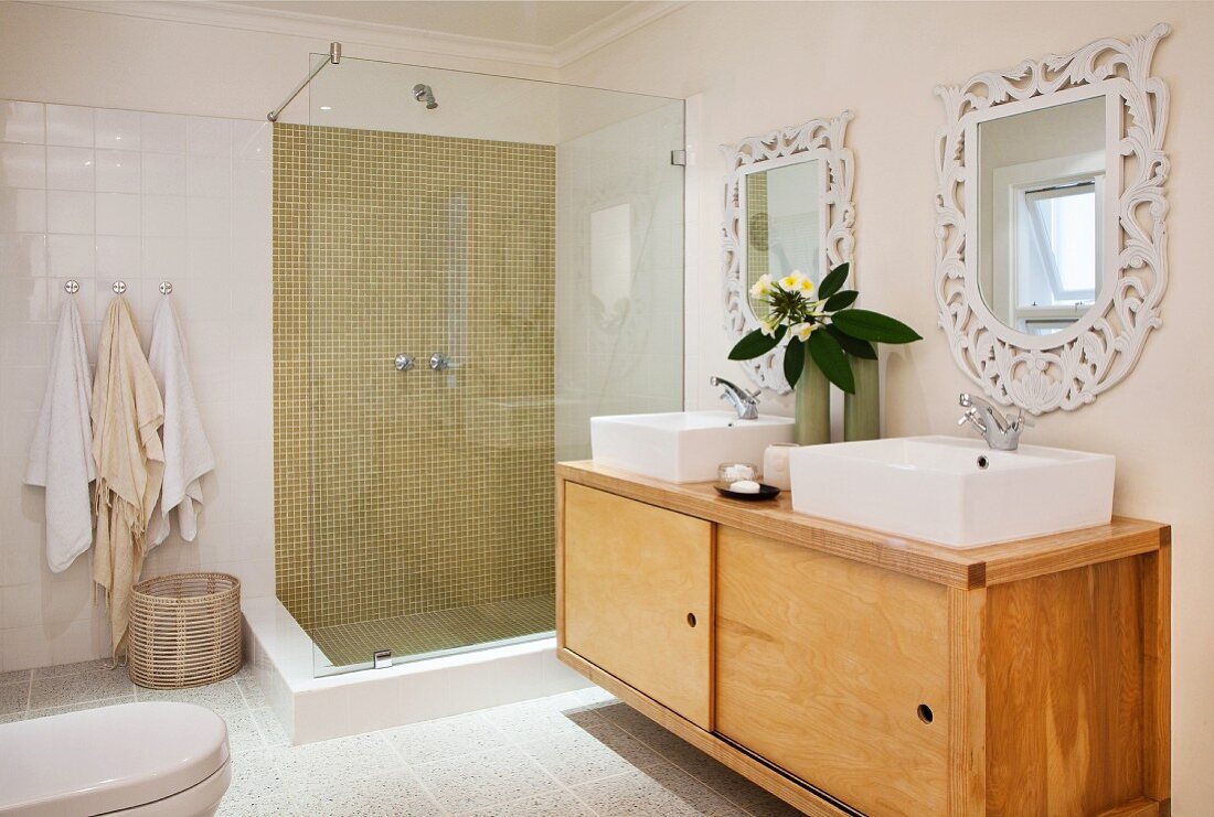 Retro, wooden sideboard with twin washbasins below mirrors on wall next to modern, glass shower cubicle