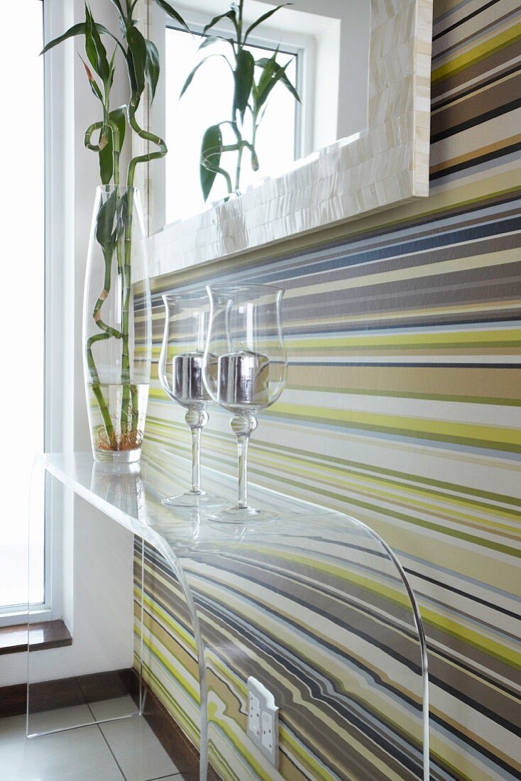 Windlichter auf Wandtisch aus transparentem Plexiglas vor Wand mit farbigen Streifen