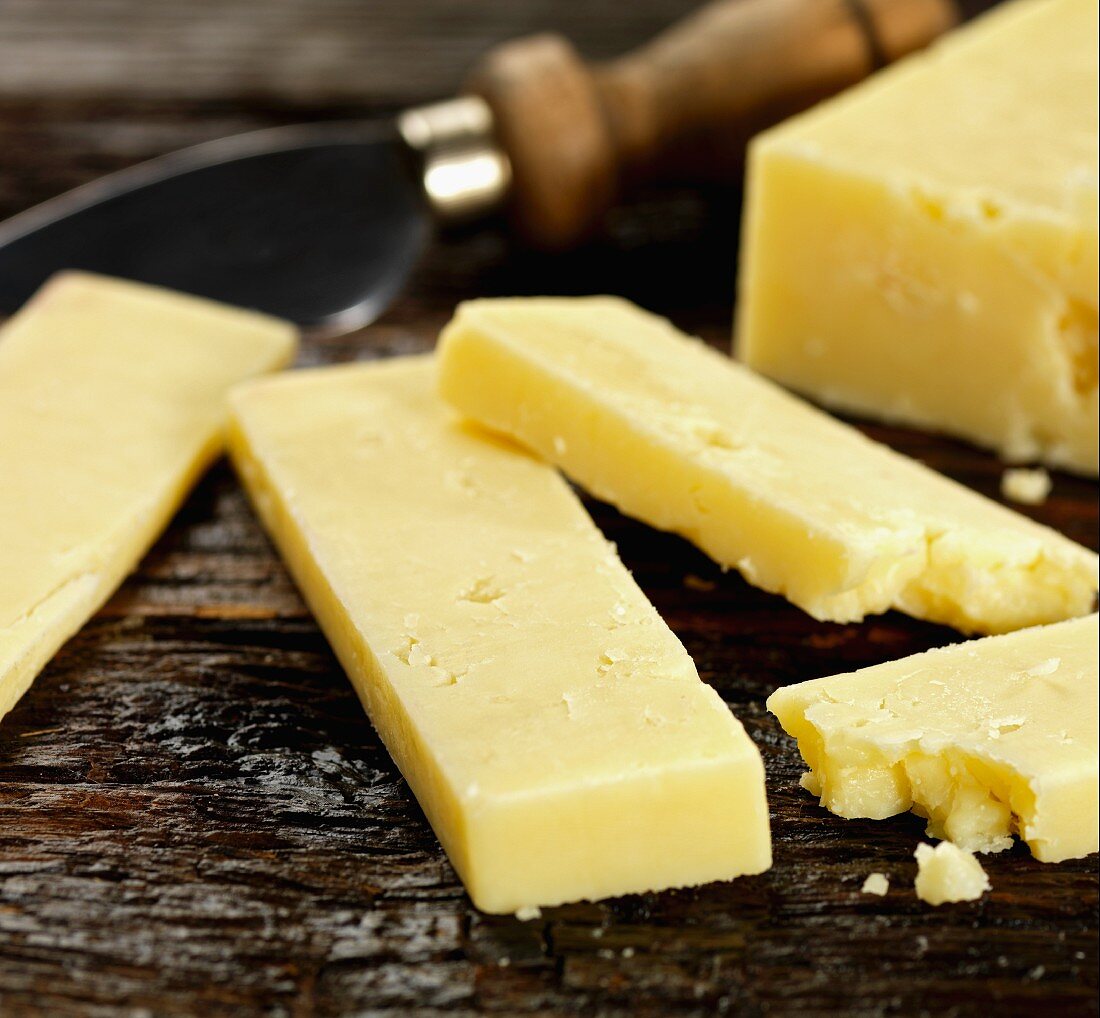 Chunks of cheddar and a cheese knife on a wooden surface