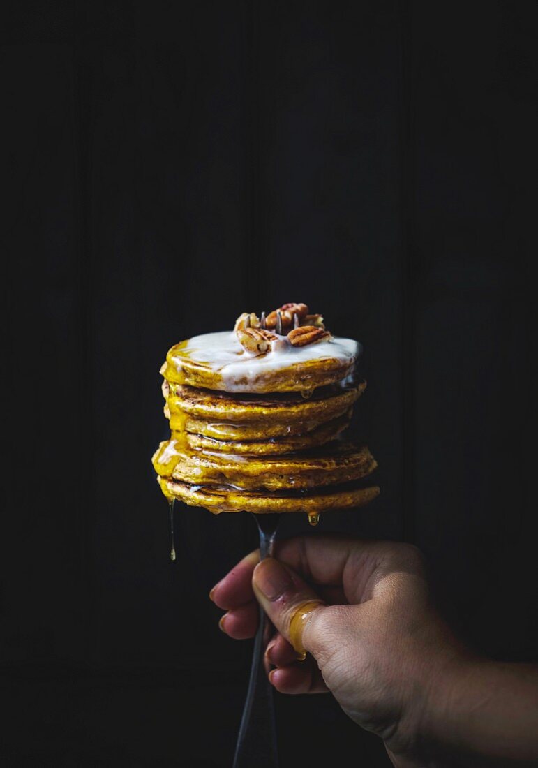 A hand holding a fork stuck into a stack of pumpkin pancakes