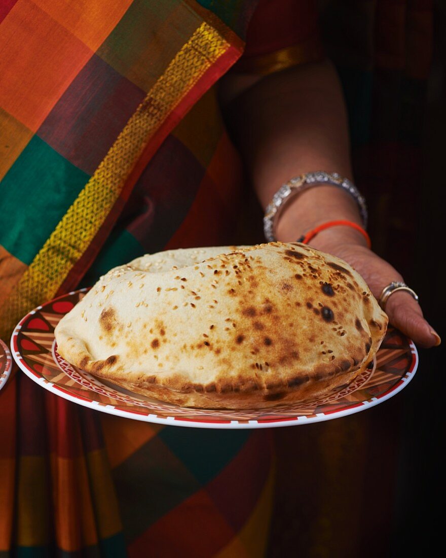 Frau hält Teller mit Käse-Naan-Brot (Indien)