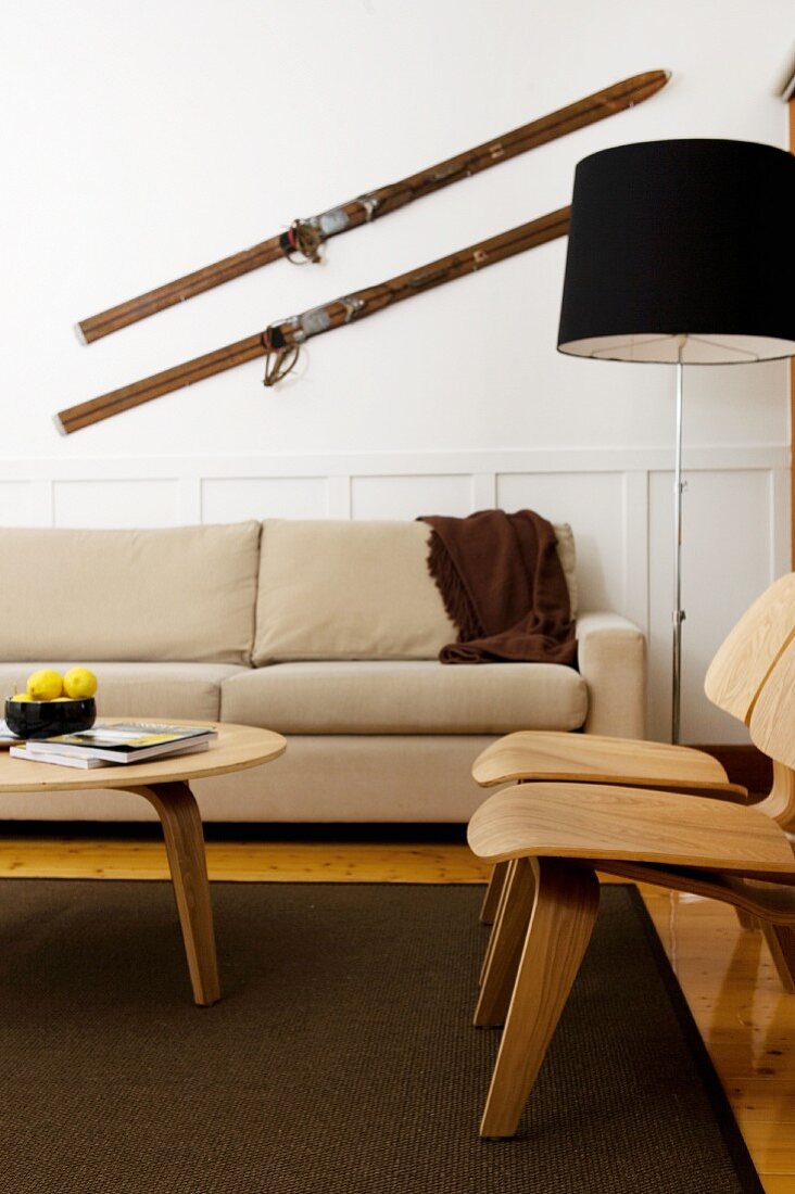 Scandinavian-style living room with beige couch, wooden chairs and antique skis on wall