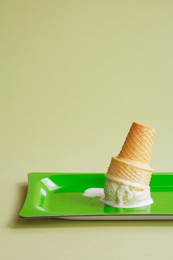 An ice cream cone with a scoop of vanilla, upturned on a green tray